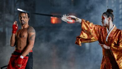 Two performers in vibrant costumes enact a martial arts scene with smoke effects.