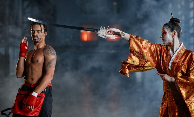 Two performers in vibrant costumes enact a martial arts scene with smoke effects.