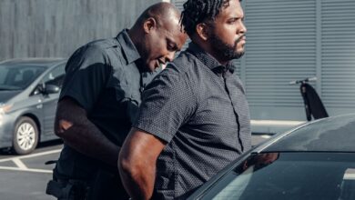 A police officer handcuffing a man next to a car in a parking lot.