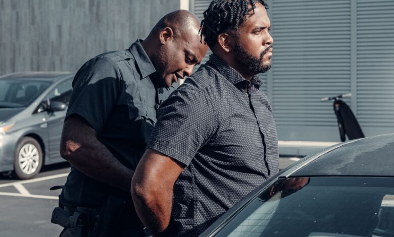 A police officer handcuffing a man next to a car in a parking lot.