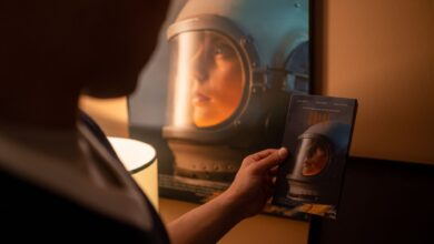 Person holding a VHS tape in front of a vintage film poster in a dimly lit room.