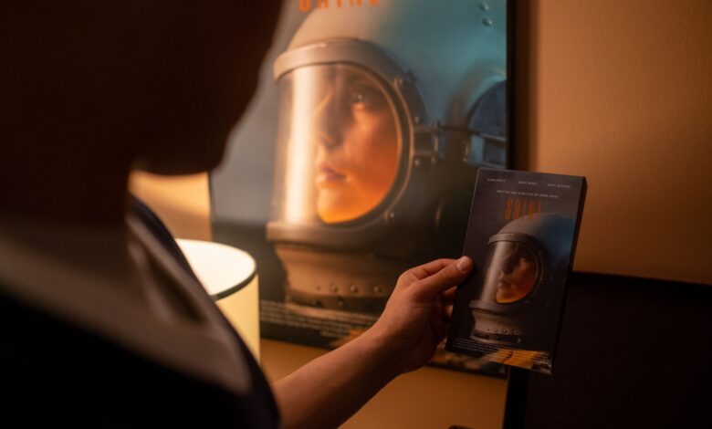 Person holding a VHS tape in front of a vintage film poster in a dimly lit room.