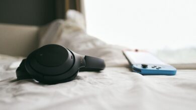 Close-up of a black headset and a gaming console resting on a soft, white bedspread in a calm, indoor setting.