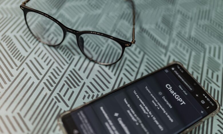 Eyeglasses next to a smartphone displaying the ChatGPT AI app on a patterned surface.