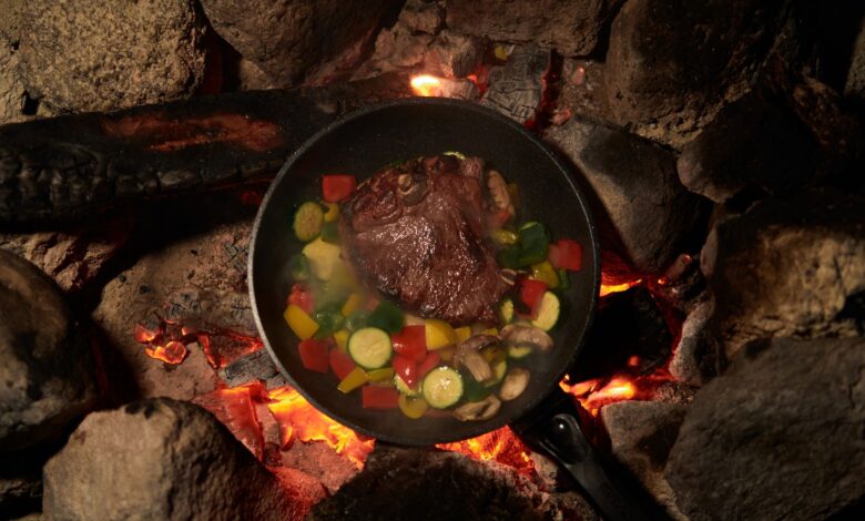 Sizzling beef steak with vegetables cooked over a campfire for an outdoor meal experience.