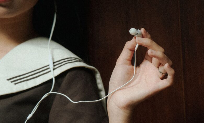 A close-up image of a hand holding earphones next to a person wearing navy attire, suggesting a relaxed mood.