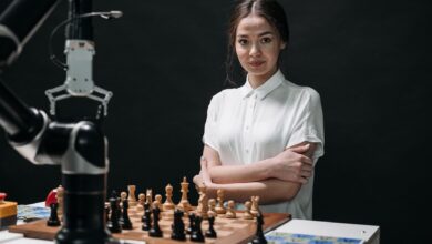 A young woman in a white blouse playing chess against a robot arm.