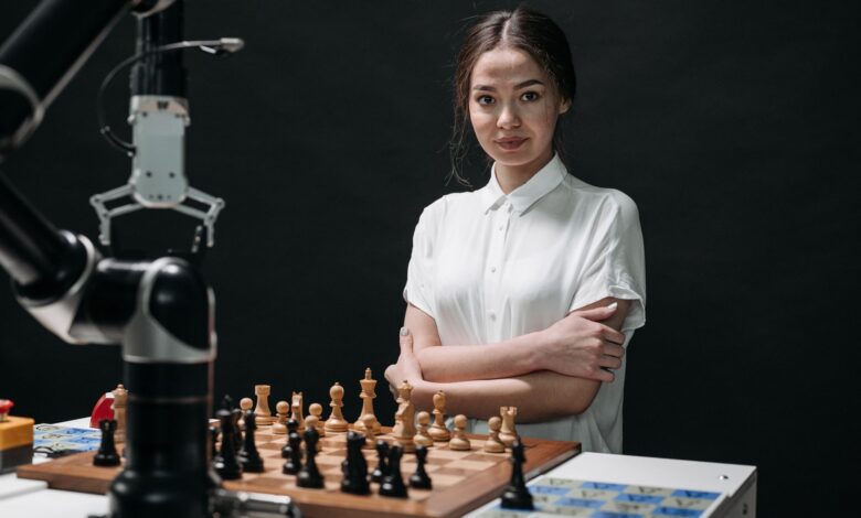 A young woman in a white blouse playing chess against a robot arm.
