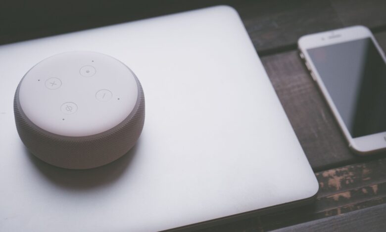 A smart speaker, laptop, and smartphone array representing modern technology lifestyle on a wooden surface.