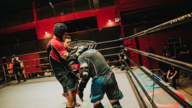 Two athletes compete in a fierce boxing match inside a well-lit indoor arena.