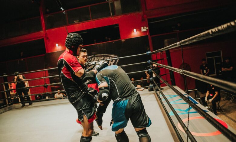 Two athletes compete in a fierce boxing match inside a well-lit indoor arena.