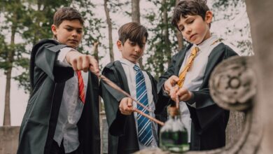 Three boys in wizard costumes casting spells with wands outdoors.