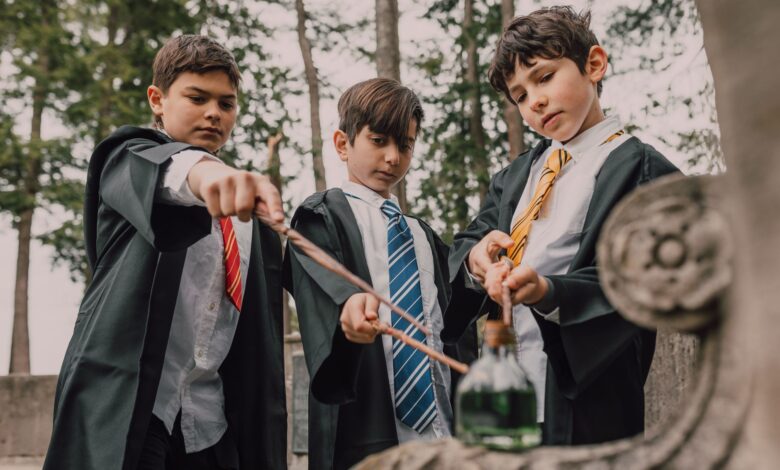 Three boys in wizard costumes casting spells with wands outdoors.