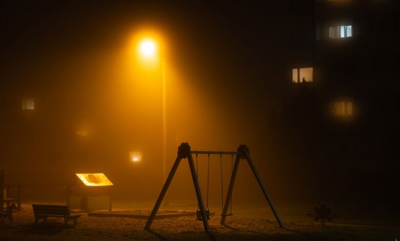 A dimly lit foggy playground under a streetlight at night, creating a mystical atmosphere.