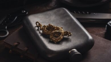 A detailed gold dragon pendant rests elegantly on a retro hip flask, set against a rustic backdrop. Perfect for artistic decor.