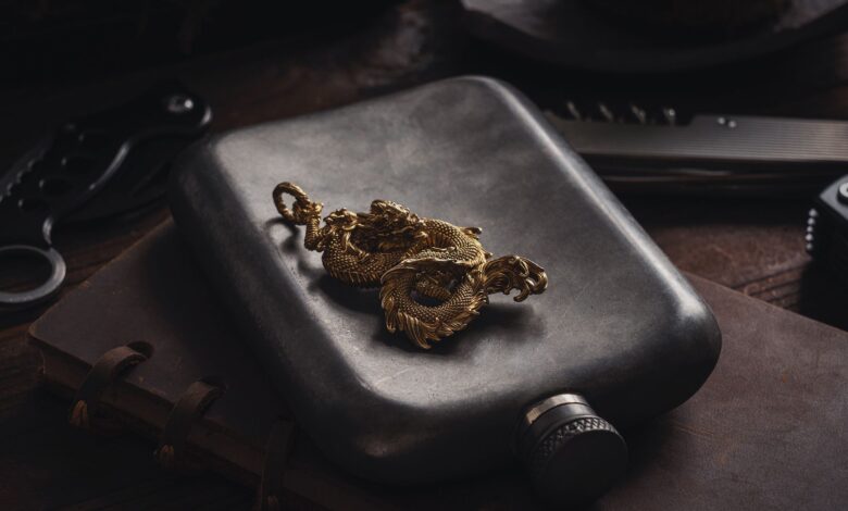 A detailed gold dragon pendant rests elegantly on a retro hip flask, set against a rustic backdrop. Perfect for artistic decor.