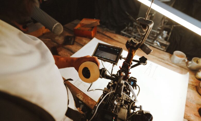 A filmmaking professional adjusting camera equipment on a wooden desk in a studio setting.