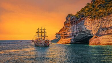 A majestic sailing ship navigates past stunning sea cliffs at sunset, offering a picturesque view of adventure.
