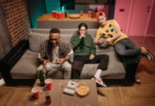 Three friends having fun gaming and drinking beer in a cozy indoor setting.