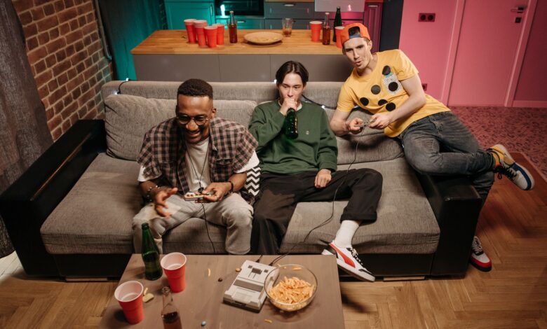 Three friends having fun gaming and drinking beer in a cozy indoor setting.