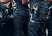 Close-up of police officers detaining a person near a car during daytime.