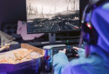 Teen playing video game with headset and drinks, indulging in pizza during gaming session.