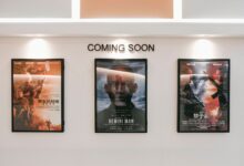 Framed posters of upcoming movies in a cinema hallway under 'Coming Soon' sign.