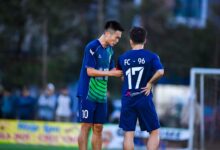 Two soccer players in blue jerseys strategize during a match in Hà Nội, Vietnam.