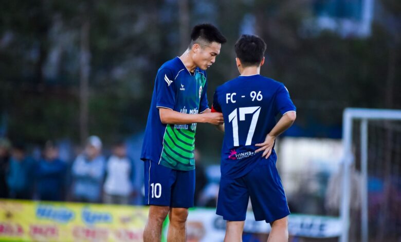 Two soccer players in blue jerseys strategize during a match in Hà Nội, Vietnam.