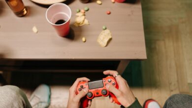 Person holding a red game controller with snacks and drinks around, top view.