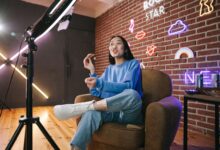 Young Asian woman streaming live indoors with neon lights, engaging audience through technology and creative content.