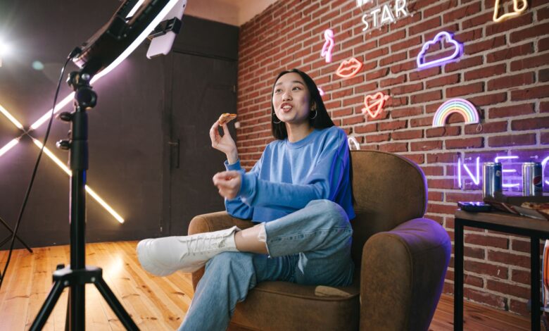 Young Asian woman streaming live indoors with neon lights, engaging audience through technology and creative content.