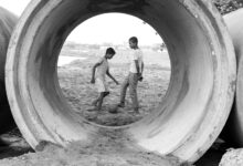 Two boys play soccer through a large cement pipe, showcasing childhood joy in urban settings.