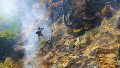Adventurous honey collector climbs rocky cliff with smoke for wild bees in Nepal.