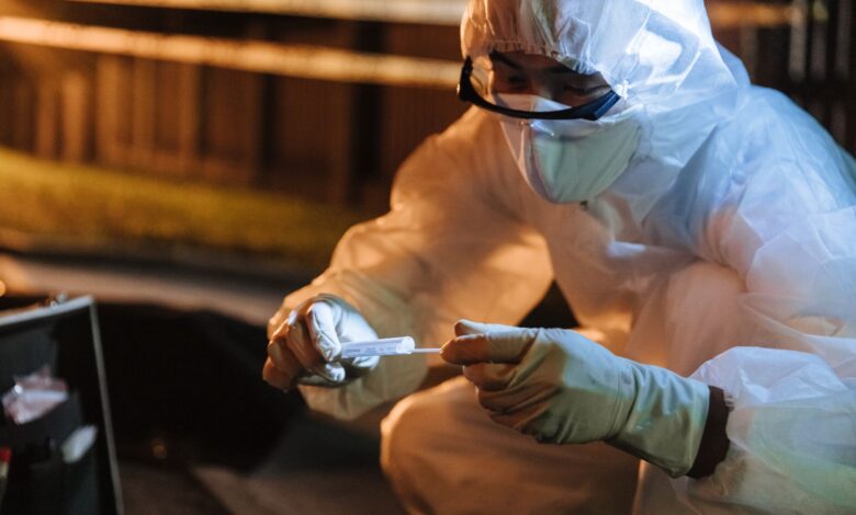 A forensic investigator in protective gear collects evidence outdoors at night.