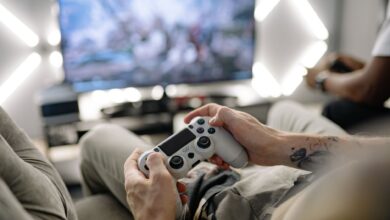 Hands holding a video game controller in a modern living room, playing on TV.