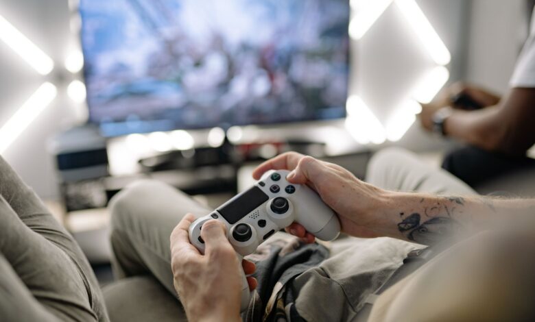 Hands holding a video game controller in a modern living room, playing on TV.