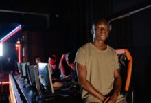A young gamer in a dimly lit gaming arena, surrounded by teammates.