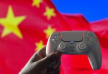 Close-up of a hand holding a PlayStation controller in front of a Chinese flag. Captured in London, UK.