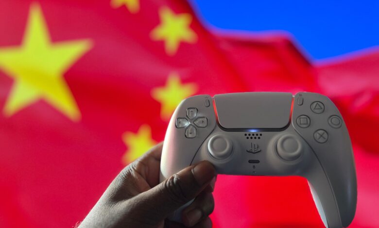 Close-up of a hand holding a PlayStation controller in front of a Chinese flag. Captured in London, UK.
