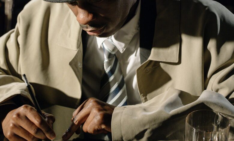 A detective in a trench coat writes notes in a noir-inspired scene with dramatic lighting.