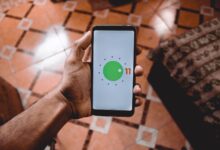Close-up of a hand holding a smartphone displaying Android 11 interface indoors on patterned floor.