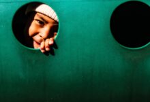 A joyful child peeping through a hole in a playground structure, playfully smiling.
