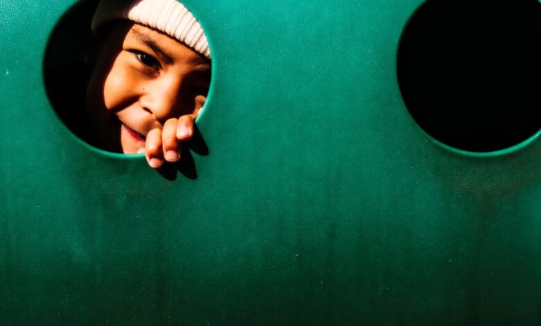 A joyful child peeping through a hole in a playground structure, playfully smiling.