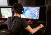 Adult male gamer immersed in PC gaming on dual monitors with headphones indoors.