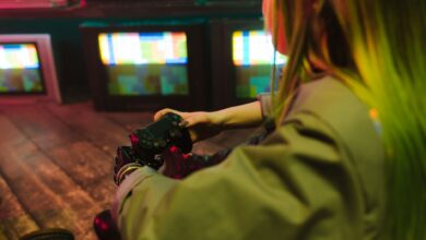 A woman with a prosthetic hand playing video games indoors amidst vintage TVs, showcasing innovation and leisure.