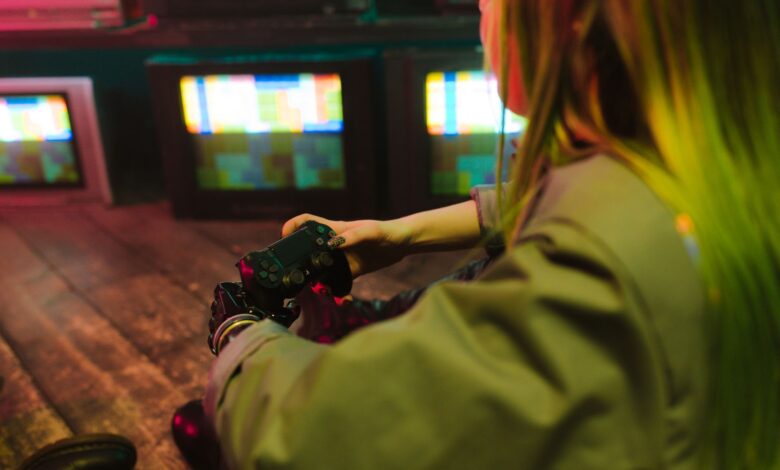 A woman with a prosthetic hand playing video games indoors amidst vintage TVs, showcasing innovation and leisure.