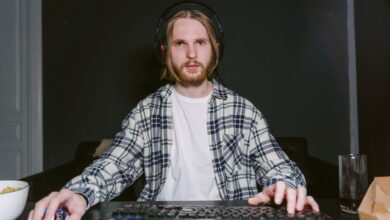 A young man focused on video gaming at home, wearing a plaid shirt and headset.