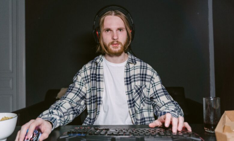 A young man focused on video gaming at home, wearing a plaid shirt and headset.