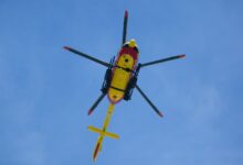 Vibrant yellow rescue helicopter soaring with rotors spinning against a clear blue sky.